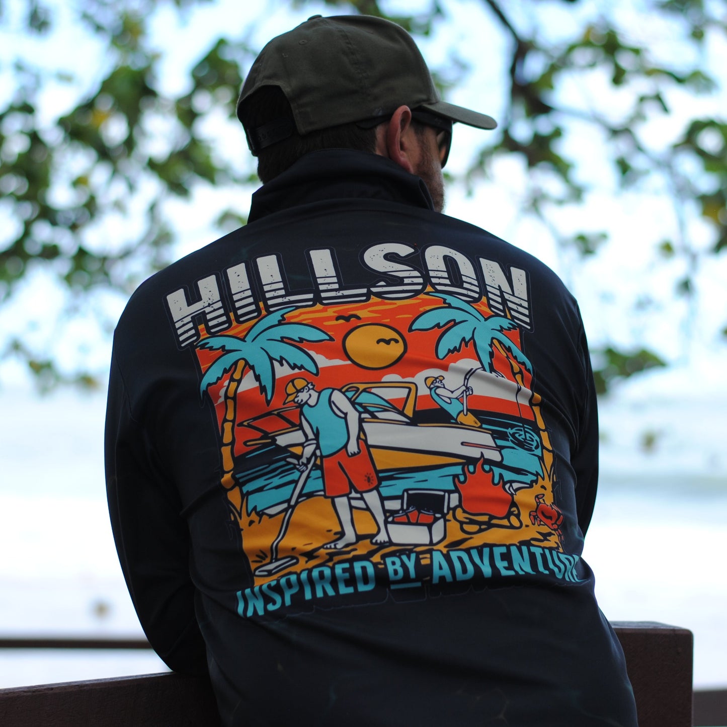 Person wearing a black hoodie with 'Hillson' and 'Inspired by Adventure' design, sitting outdoors.