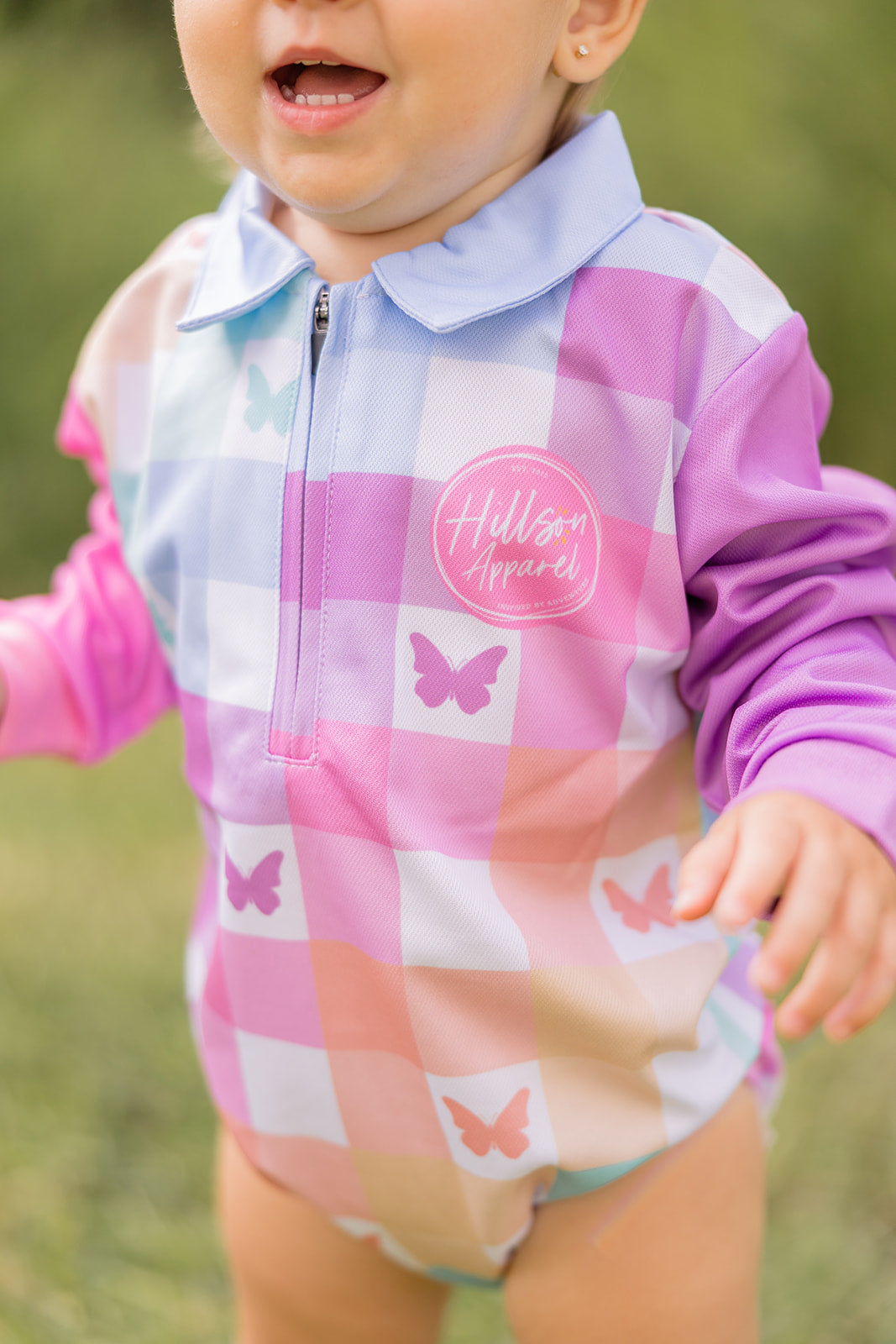 Child wearing a colourful checkered fishing romper outfit with butterfly designs outdoors