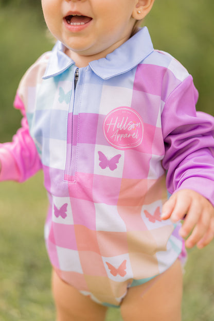 Child wearing a colourful checkered fishing romper outfit with butterfly designs outdoors
