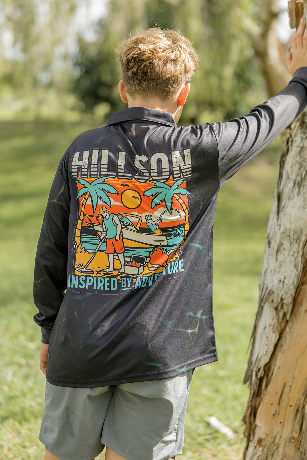 Person wearing a lightweight fishing shirt with colourful graphics and text, standing outdoors near trees.