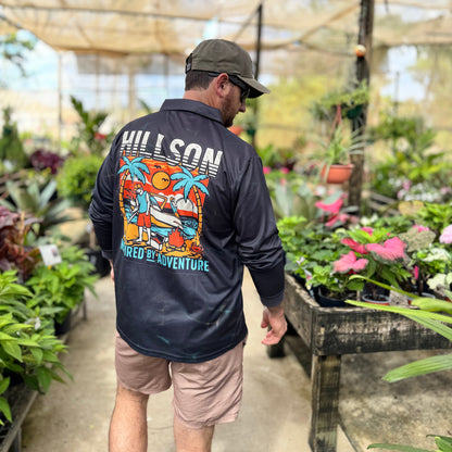 Man wearing a black fishingshirt with colorful graphics and text in a greenhouse setting